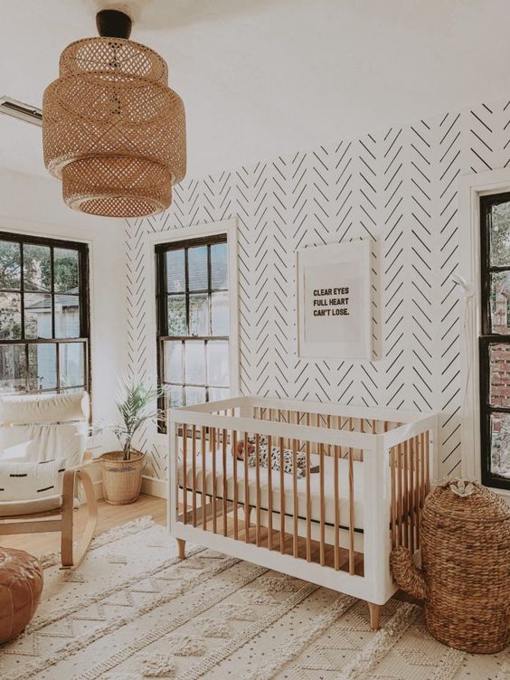 a welcoming boho nursery with a printed wall, white and stained furniture, a cactus basket for storage, neutral textiles and a woven pendant lamp