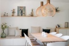an airy contemporary dining room with a built-in storage bench, pillows, a light-stained table and white chairs, pendant plywood lamps
