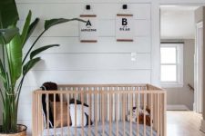 an airy modern tropical nursery with a stained floor, planked walls, a light stained crub, prints and a potted statement plant
