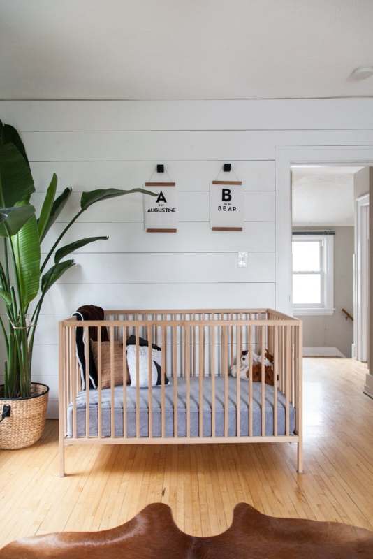 an airy modern tropical nursery with a stained floor, planked walls, a light stained crub, prints and a potted statement plant