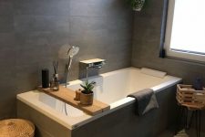 an elegant bathroom clad with taupe tiles, a bathtub clad with them, some potted greenery, baskets and crates for storage
