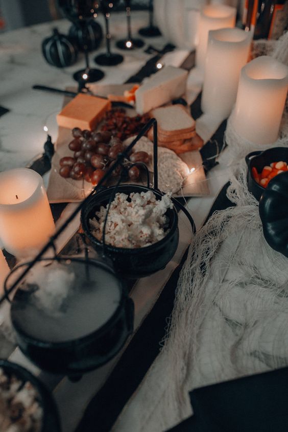 a cool Halloween table with cauldrons used to serve various sweets like popcorn is a very fresh and stylish idea for Halloween