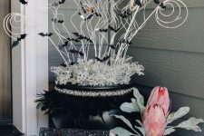 11 crazy Halloween front porch decor with a spellbook, a black planter with oversized blooms, a black cauldron with twigs and black bats