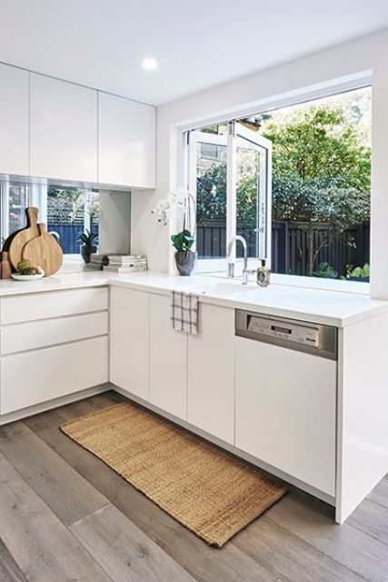 a minimalist white kitchen with sleek cabinets, a window backsplash and a folding window for fresh air or as a pass through window