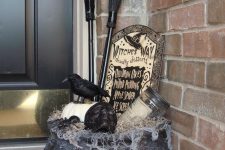 17 a Halloween porch decoration of an old witch cauldron with a pumpkin, a skull, a jar, a tombstone, a blackbird and some witches’ brooms