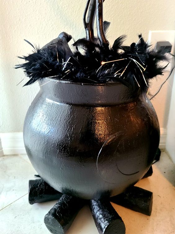 a lovely Halloween decoration of a black cauldron with feathers and lights, black firewood is a cool solution you can DIY