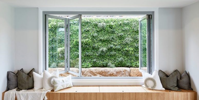 a folding window with a built-in storage daybed with lots of pillows and a greenery view is a gorgeous idea for a modern space