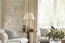 a French farmhouse living room in neutrals with a large arched French window, neutral furniture, a low coffee table and greenery