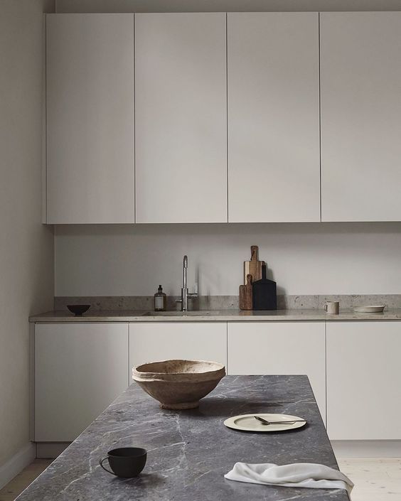 a Nordic greige kitchen with sleek cabinets, a neutral stone countertop, a grey stone table and pretty tableware