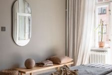 a beautiful greige bedroom with a bed with neutral and printed bedding, a wooden bench, warm-colored textiles, a paper pendant lamp and a basket for storage