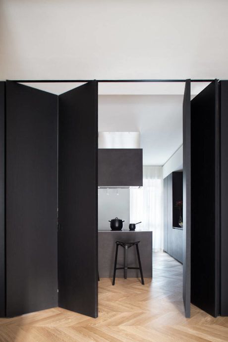 a black folding door matches the minimalist space and the color palette and makes a bold statement in the house