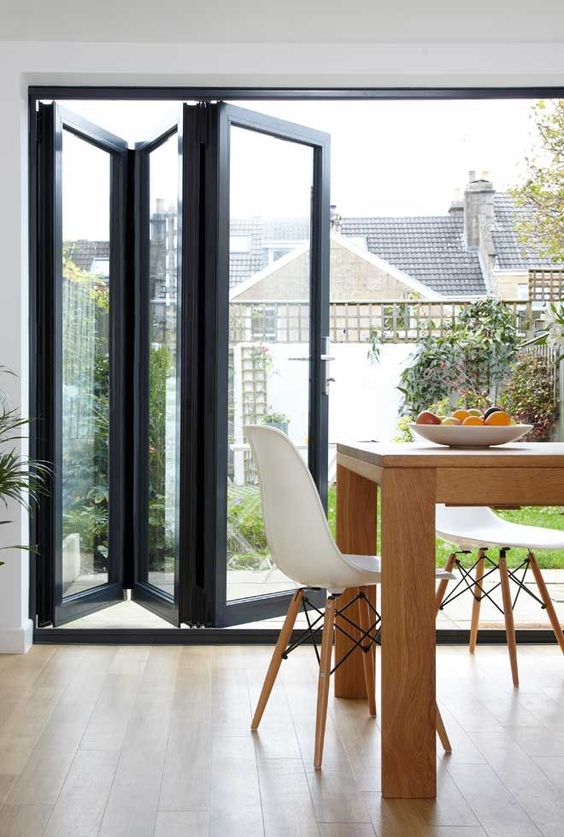 a black frame glass folding door separates the dining room from the garden and lets enjoy the views and natural light and lets an easy access to the garden