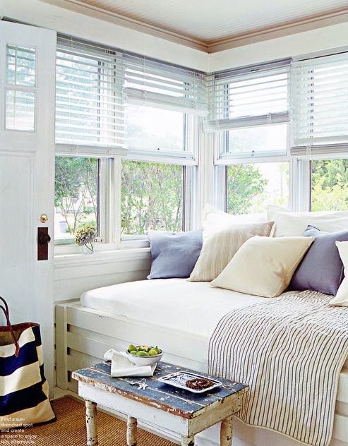 a bright and fresh windowsill reading nook with a built-in daybed with pillows and a shabby chic table