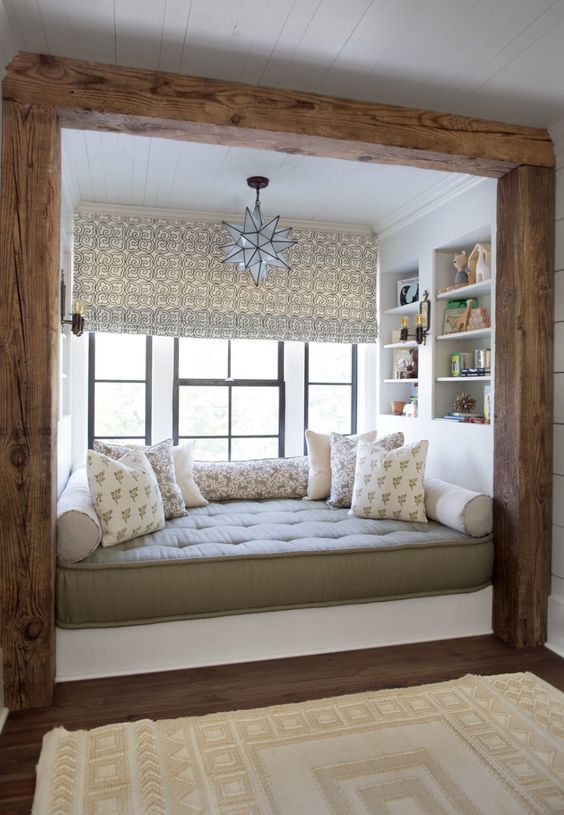 a cabin chic windowsill reading nook with a large upholstered daybed, some printed pillows and built-in bookshelves