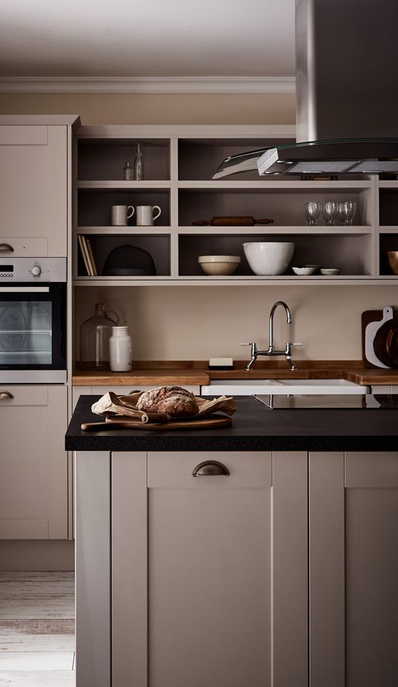 a catchy greige kitchen with shaker cabinets, black and butcherblock countertops, an open storage cabinet, modern appliances and vintage fixtures