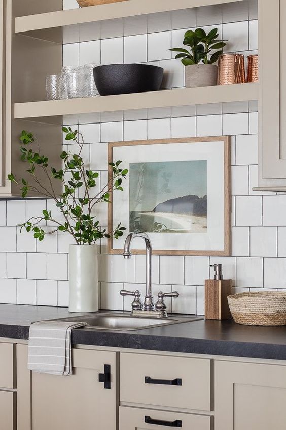 a catchy greige kitchen with shaker cabinets, built-in shelves, black handles, a white square tile backsplash and black stone countertops