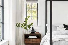 a chic bedroom in white and grey, with a black canopy bed and black French windows, neutral textiles and black lamps