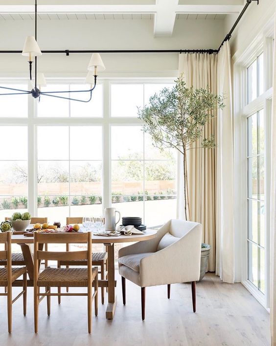 a chic neutral dining room with French windows, a trestle wooden table, woven chairs, a chic chandelier and neutral curtains is amazing