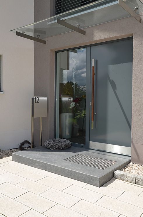 a contemporary entrnace with a grey metal front door with an oversized handle and a window on the left is a cool idea