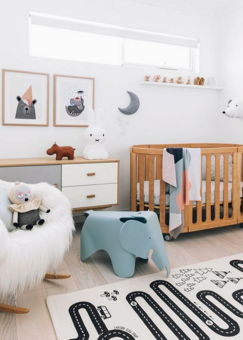 a cozy Scandi nursery with a stained crib, a stained dresser, a faux fur chair, a blue elephant chair, some artworks and a play rug