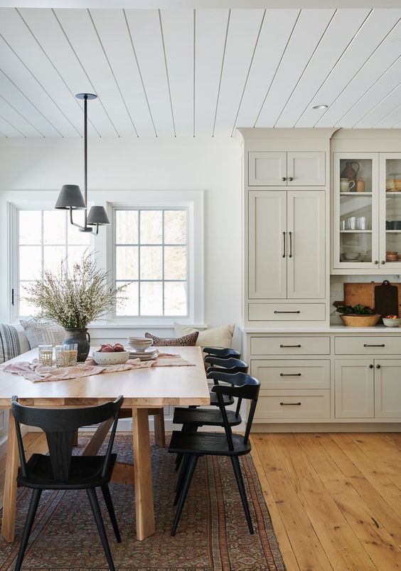 a cozy farmhouse kitchen with a dining space, French windows, neutral cabinetry, a butcherblock table and black chairs, a black pendant lamp