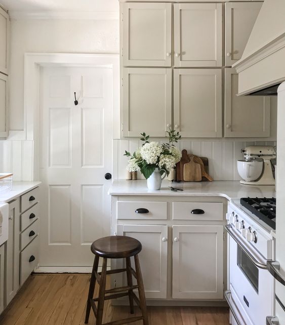 a delicate greige kitchen with shaker cabinets, a white planked backsplash, vintage appliances and black and neutral fixtures is amazing