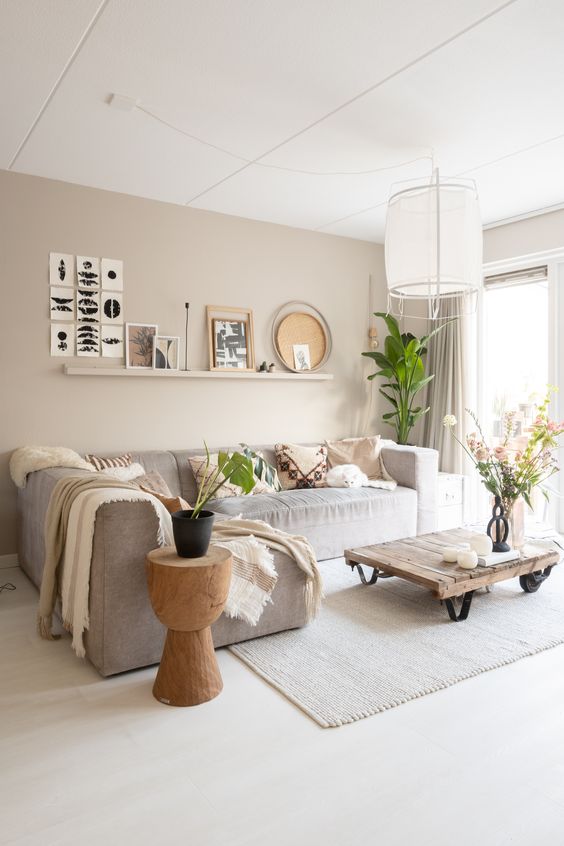a delicate greige living room with a long ledge with a gallery wall, a grey sectional, an industrial coffee table and a wooden side table