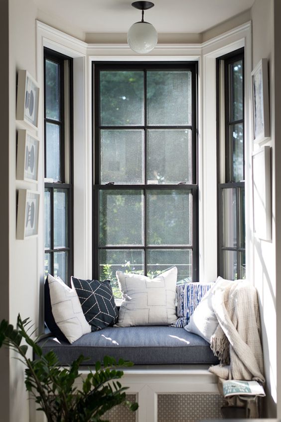 a double-height bow window with a small windowsill and a built-in seat with a cushions and pillows is a lovely nook to spend time