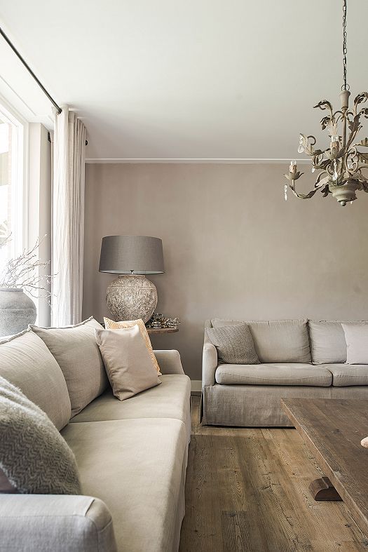 a dreamy greige living room with neutral sofas, a catchy chandelier, a table lamp and a large vase with branches plus a wooden coffee table