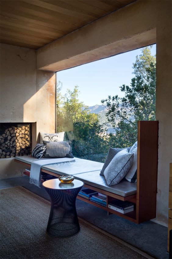a gorgeous windowsill reading space with a leather couch, open bookshelves and pillows by a panoramic window