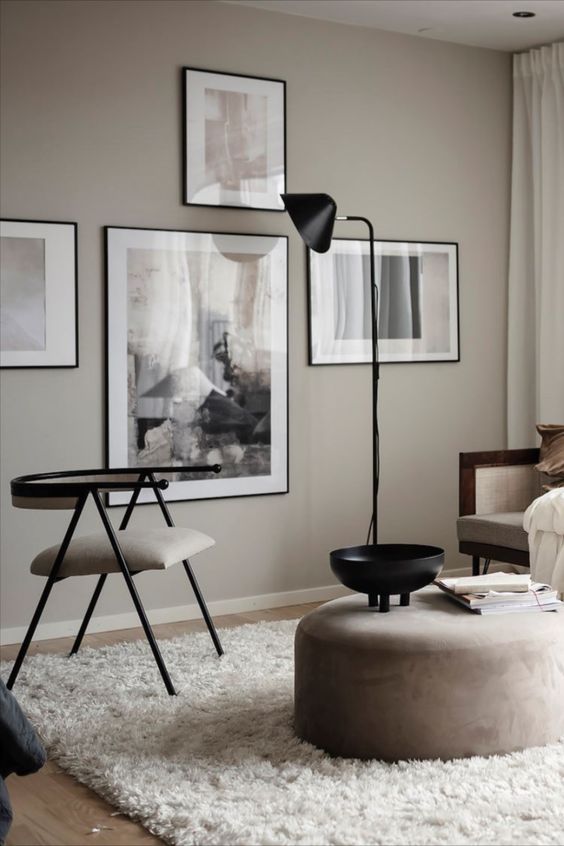 a greige Scandi-inspired living room with a cool gallery wall, neutral seating furniture, a round pouf, a cool rug and a black floor lamp