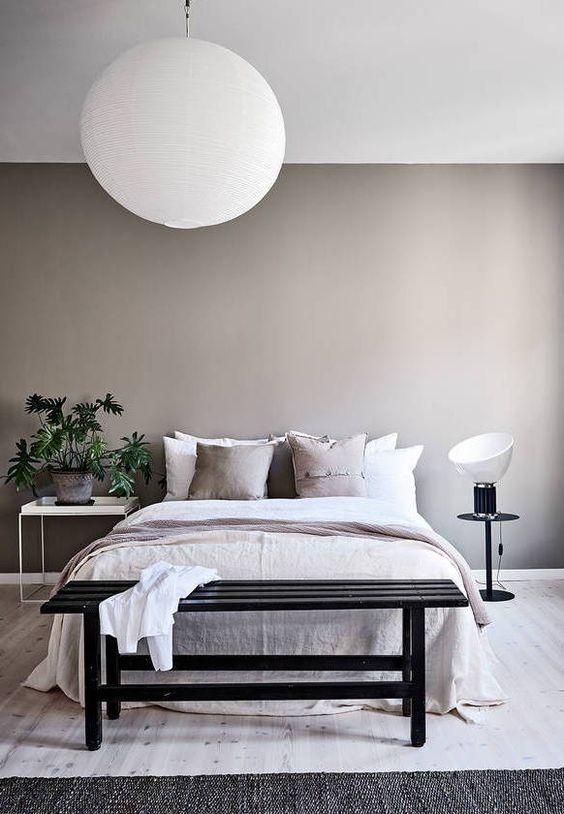 a greige bedroom with a pretty bed, mismatching nightstands, a potted plant, a black bench and neutral bedding is amazing