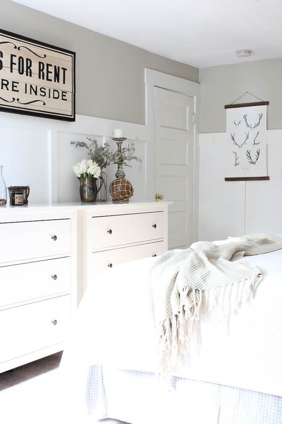 a greige farmhouse bedroom with white paneling, white furniture and textiles, mini artworks and some pretty decor and accessories