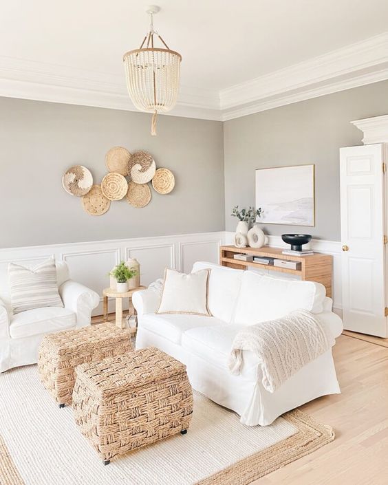 a greige farmhouse living room with paneling, white seating furniture, woven storage poufs, decorative baskets and a credenza is a chic space