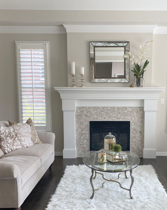 a greige living room with a built-in fireplace, a neutral sofa, a creamy rug, a coffee table, a mirror and some candles is a lovely idea
