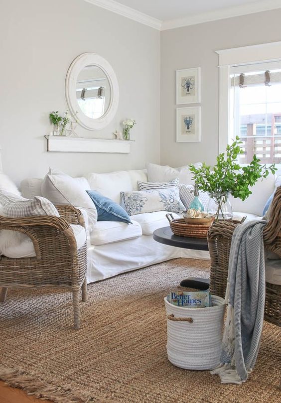 a lovely greige farmhouse living room with a white sectional, woven chairs, a mini gallery wall, a round mirror and printed pillows