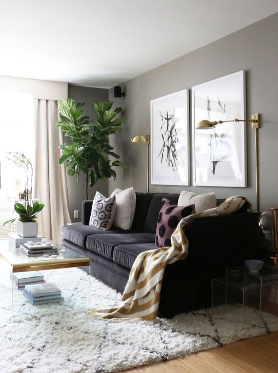 a lovely greige living room with a black sofa, a mini gallery wall, gold sconces, acrylic side tables and a coffee table plus statement plants