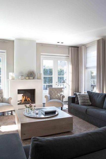 a lovely greige living room with greige textiles, a fireplace, graphite grey sofas, a wooden coffee table and elegant creamy chairs