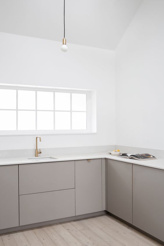 a minimalist greige kitchen with sleek cabinets, white stone countertops, brass touches and white walls is amazing