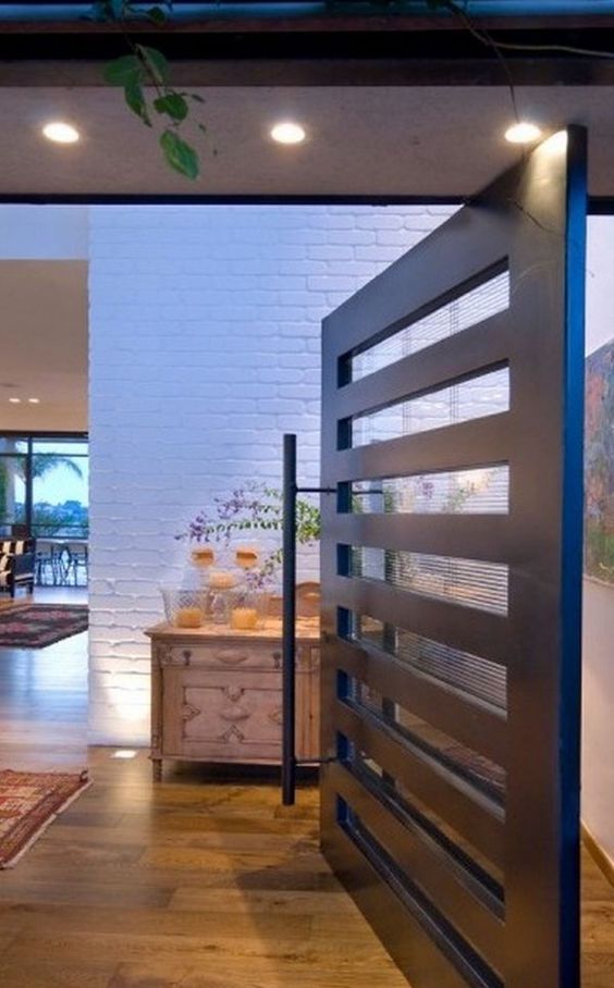 a modern blackened metal pivot door with frosted glass inserts and an oversized handle is a cool idea for a modern house