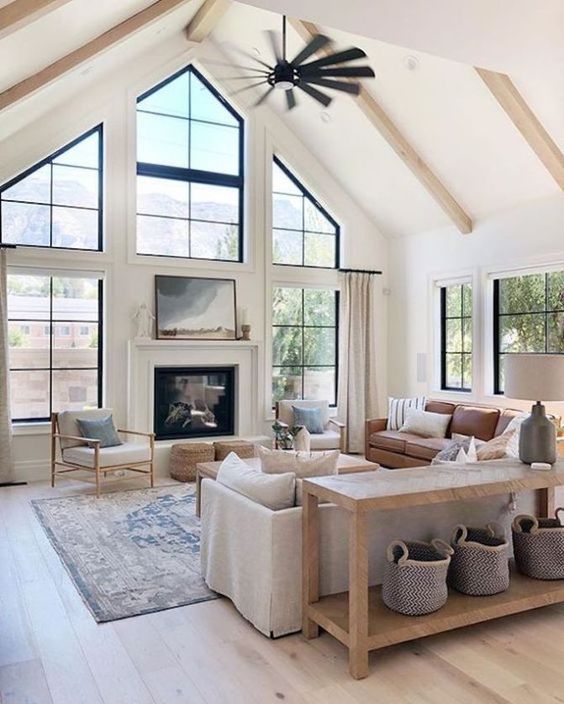 a modern farmhouse living room in neutrals, with black framed French windows, a built in fireplace, neutral furniture and a wooden console table