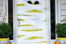 a neon neon yellow door styled as a mummy, with pumpkins in planters around is a lovely and playful solution for Halloween