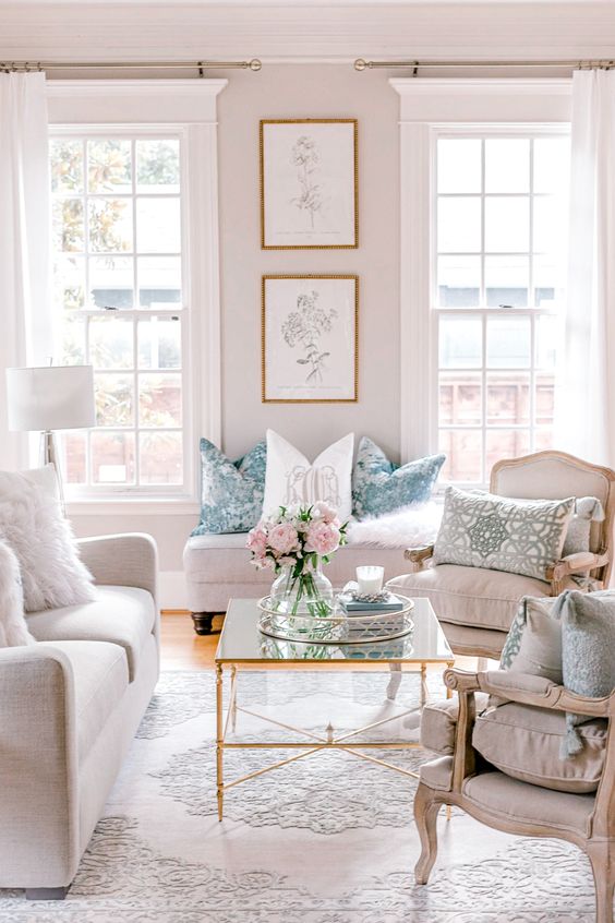 a pretty and welcoming neutral living room with tall French windows, refined vintage furniture, a glass coffee table and printed pillows