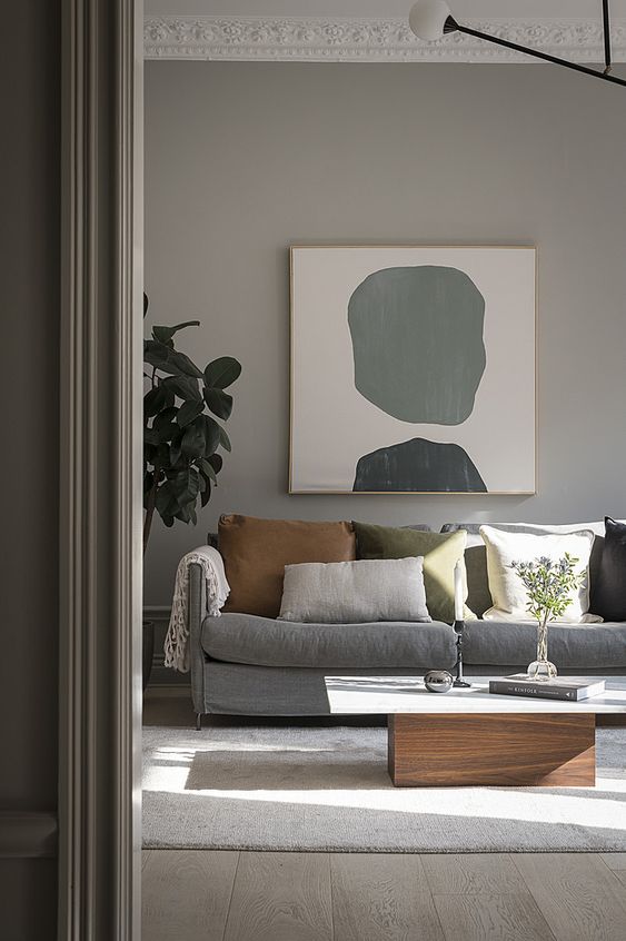 a pretty greige living room with a grey sofa, a low coffee table, muted color pillows, an abstract artwork and a statement plant