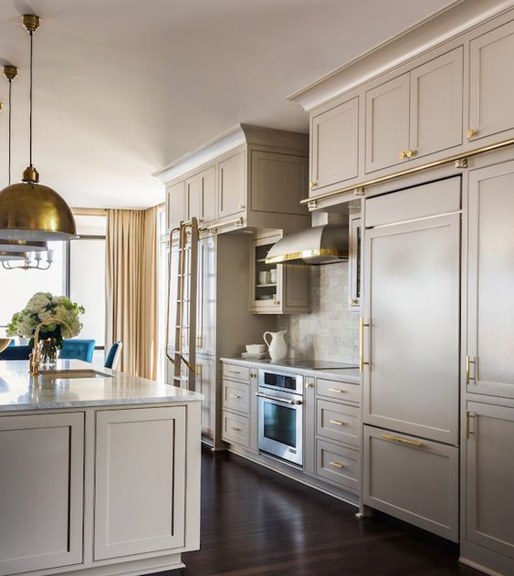 a pretty modern greige kitchen with shaker cabinets, neutral stone countertops and a backsplash, gold handles and gold pendant lamps
