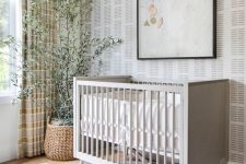 a relaxed Scandinavian nursery with printed wallpaper, a grey crib, an artwork, a mobile, a potted tree, layered rugs and striped curtains