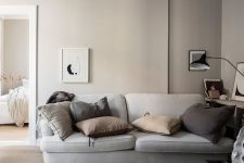a relaxing greige living room with a grey sofa, muted color pillows, a bookshelf, some artworks and a black table lamp