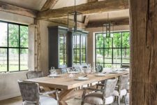 a rustic vintage dining space with wooden beams, a black buffet, a wooden trestle table, grey chairs and pendant lamps