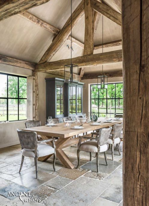 a rustic vintage dining space with wooden beams, a black buffet, a wooden trestle table, grey chairs and pendant lamps