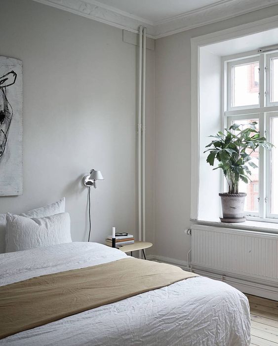 a serene bedroom with greige walls, a bed with neutral bedding, wooden nightstands, potted plants and an abstract artwork is wow